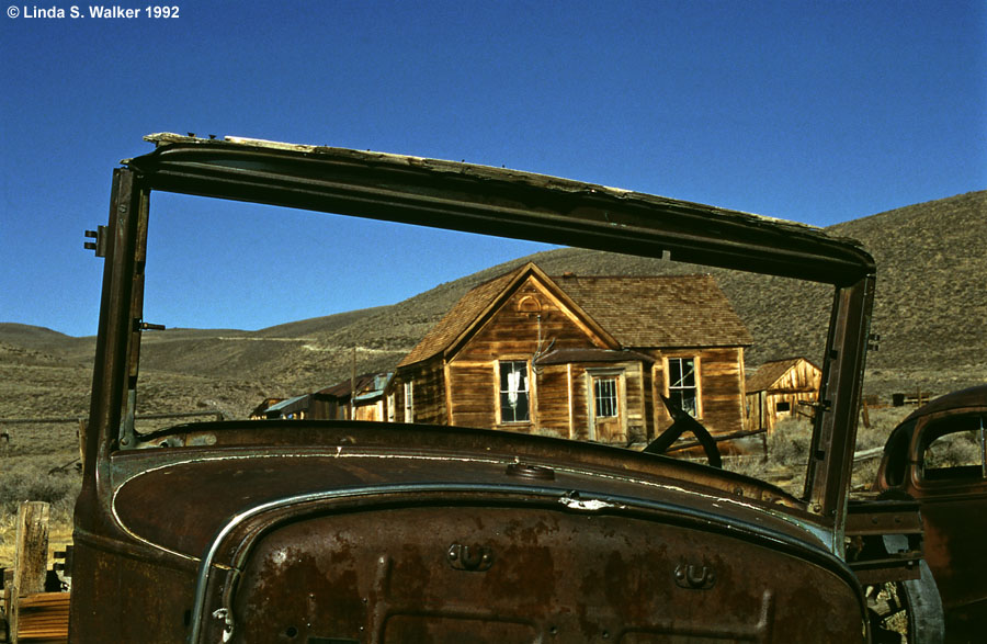 An old house is framed by the windshield of a derelict car, Bodie, California