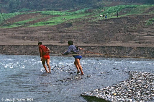 Two crewmen pull a boat through the shallow Shengdong River, China